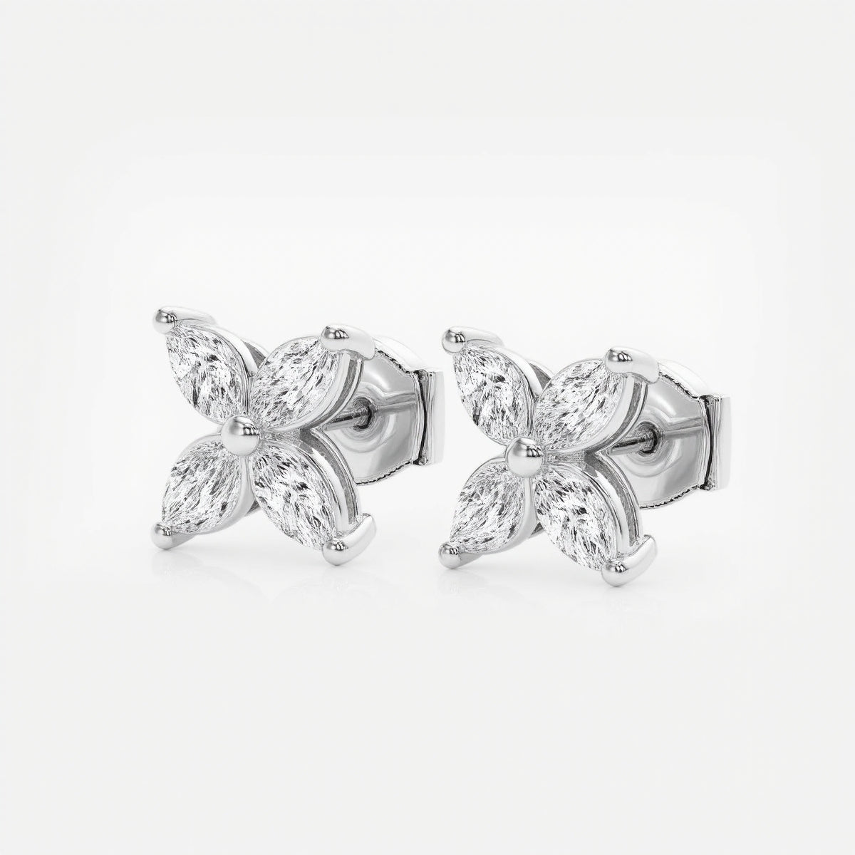 A pair of stud earrings crafted in white gold features two four-petaled floral motifs, each petal formed by a sparkling marquise-cut diamond set around a tiny polished gold bead. The cool silver tones of the metal perfectly complement the clear brilliance of the diamonds, creating a refined yet eye-catching silhouette. The earrings lie side by side on a seamless white background under bright, even studio lighting, highlighting their mirror-shiny finish and crisp faceted sparkle.