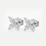 A pair of stud earrings crafted in white gold features two four-petaled floral motifs, each petal formed by a sparkling marquise-cut diamond set around a tiny polished gold bead. The cool silver tones of the metal perfectly complement the clear brilliance of the diamonds, creating a refined yet eye-catching silhouette. The earrings lie side by side on a seamless white background under bright, even studio lighting, highlighting their mirror-shiny finish and crisp faceted sparkle.