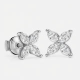 A pair of stud earrings in white gold features eight marquise-cut diamonds\u2014four per earring\u2014arranged symmetrically as a four-petal flower around a polished round center. Each diamond petal is secured by discreet prongs that emphasize the delicate floral motif. They sit side by side against a seamless white background under bright, even studio lighting that accentuates the metal\u2019s sheen and the stones\u2019 brilliance in a clean, high-key photographic style.