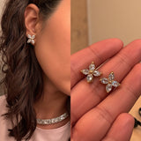A single gold stud earring featuring four marquise-cut clear gemstones arranged in a cross shape is set in yellow gold. It is worn on the model\u2019s left earlobe and displayed in a tight profile headshot with dark hair pulled back. Soft, even lighting accentuates the sparkle of the stones against the wearer\u2019s smooth skin and white collar. The neutral background and crisp focus give the image a minimalist, editorial feel. | Adorn By You